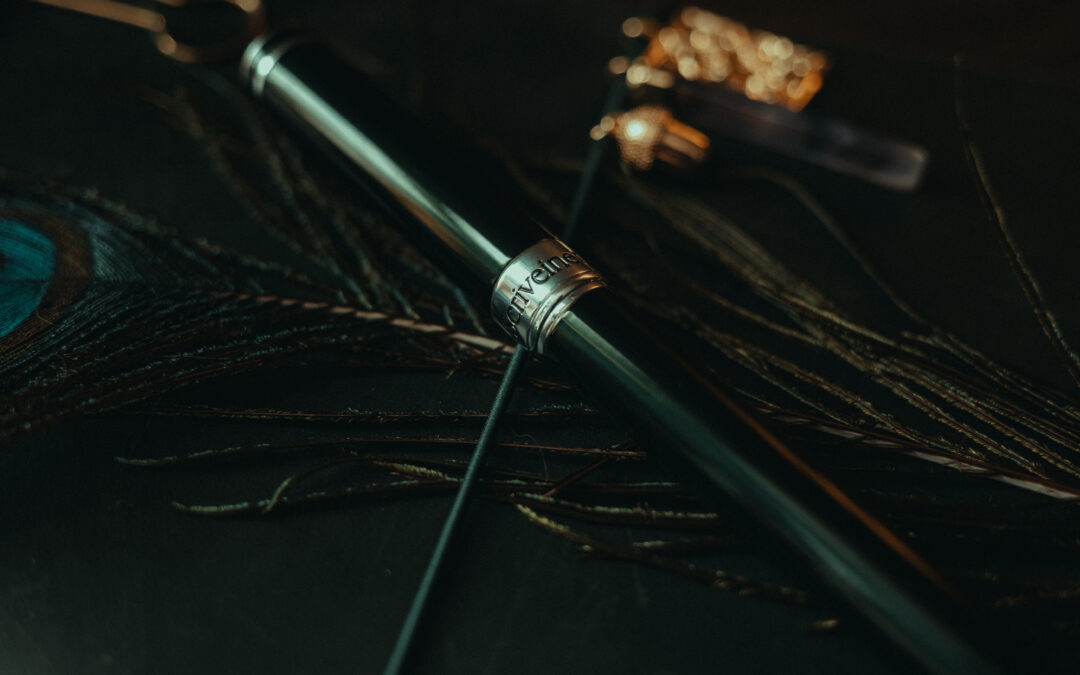 Close-up of a green Scrivener fountain pen resting on a peacock feather, photographed in low light with shallow depth of field.